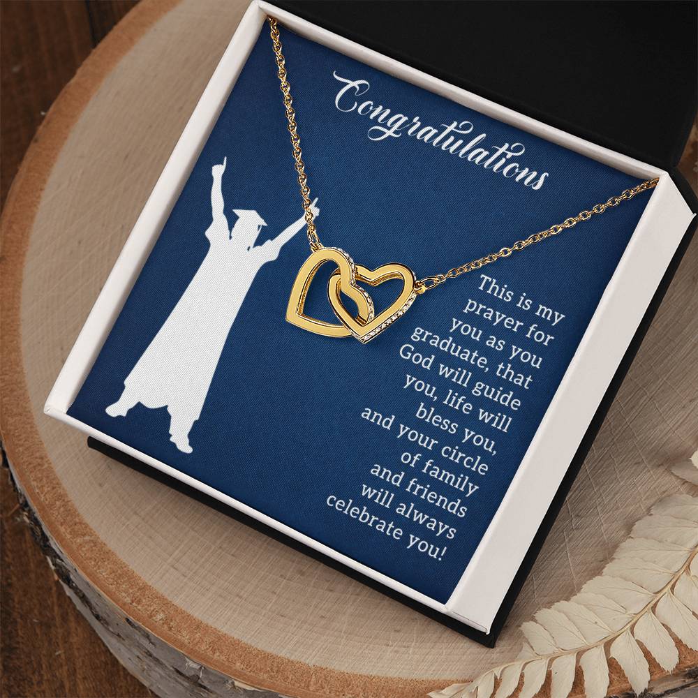 A ShineOn Fulfillment "Prayer For Graduation - Interlocking Hearts Necklace" with interlocking hearts in a gift box featuring a graduation-themed inscription and the silhouette of the Statue of Liberty.