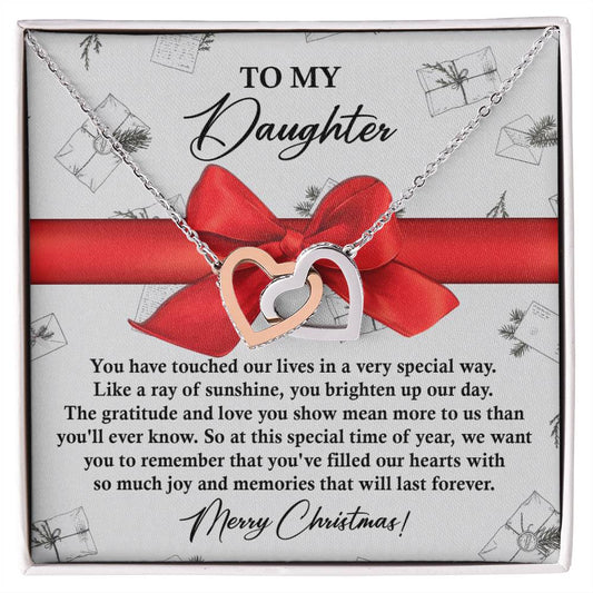 The Daughter-Special Way - Interlocking Hearts Necklace, featuring a heart-shaped design with a rose gold finish and sparkling cubic zirconia crystals, is beautifully presented on a card with a Christmas message for your daughter. It is adorned with a red bow and set against a decorative background.