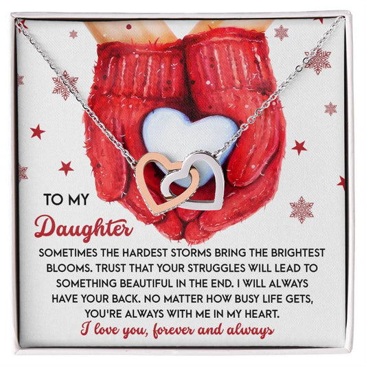 The "Daughter-In My Heart - Interlocking Hearts Necklace" is adorned with sparkling cubic zirconia crystals and rests on a card showcasing red mittens holding a heart. The heartfelt message to a daughter expresses love and support, beautifully complemented by the necklace's rose gold finish.