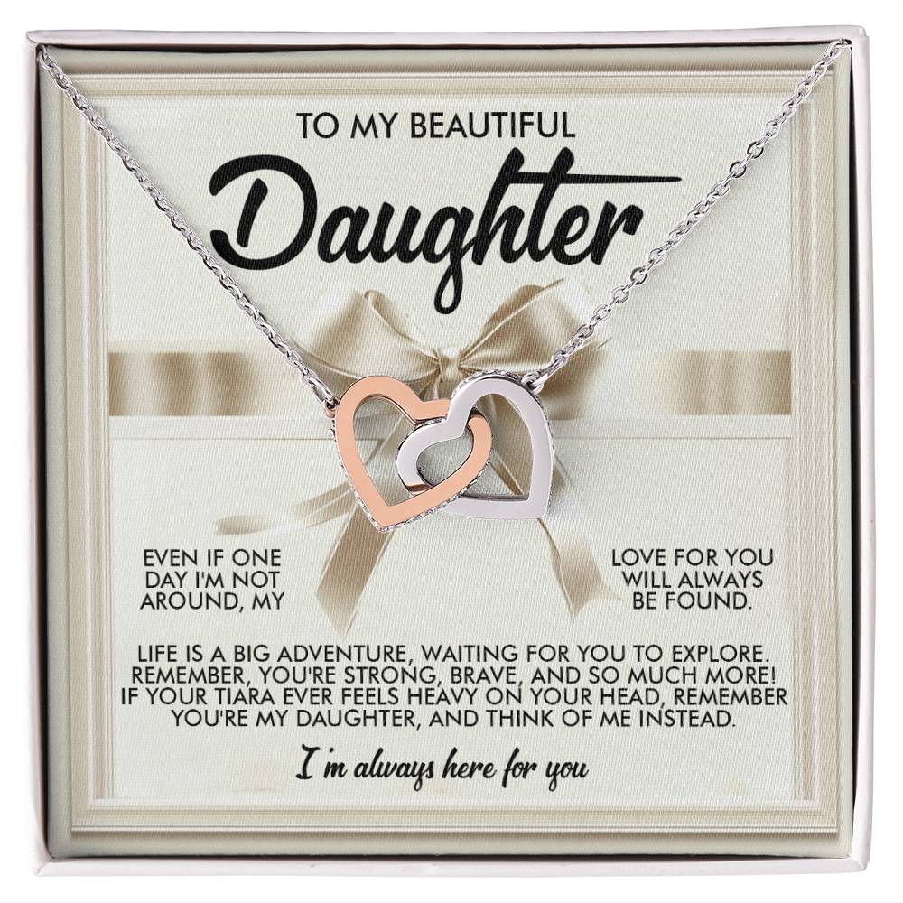 The Daughter-Heavy Tiara - Interlocking Hearts Necklace showcases intertwined silver heart pendants adorned with cubic zirconia crystals. It comes on a padded card with a heartfelt message for a daughter and includes a decorative ribbon on the beige background, embodying love and support.