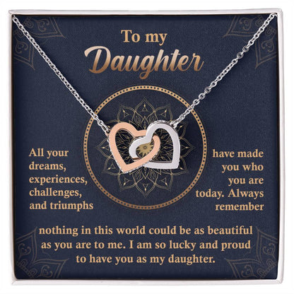 A "To My Daughter, All Your Dreams - Interlocking Hearts Necklace" with a rose gold finish and sparkling cubic zirconia crystals sits in a display box, accompanied by a heartfelt message expressing a parent's pride and love for their daughter.