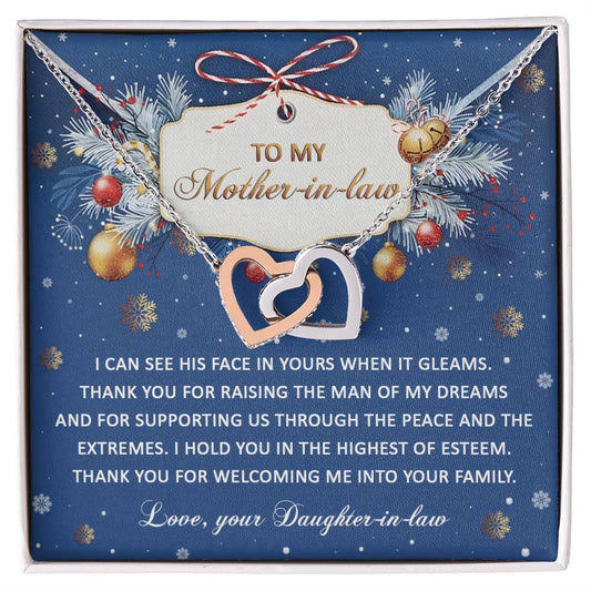 The Mother-in-law-I Hold You - Interlocking Hearts Necklace is crafted from surgical steel and adorned with cubic zirconia crystals. It comes on a card that reads, "To my Mother-in-law," featuring a heartfelt message of gratitude from a daughter-in-law. The festive background showcases pine branches and ornaments.