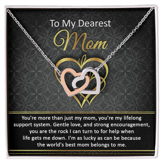 A heart-shaped pendant necklace featuring the To Mom, Belongs To Me2 - Interlocking Hearts Necklace, displayed on a floral background with a heartfelt message to 'mom' inscribed above.