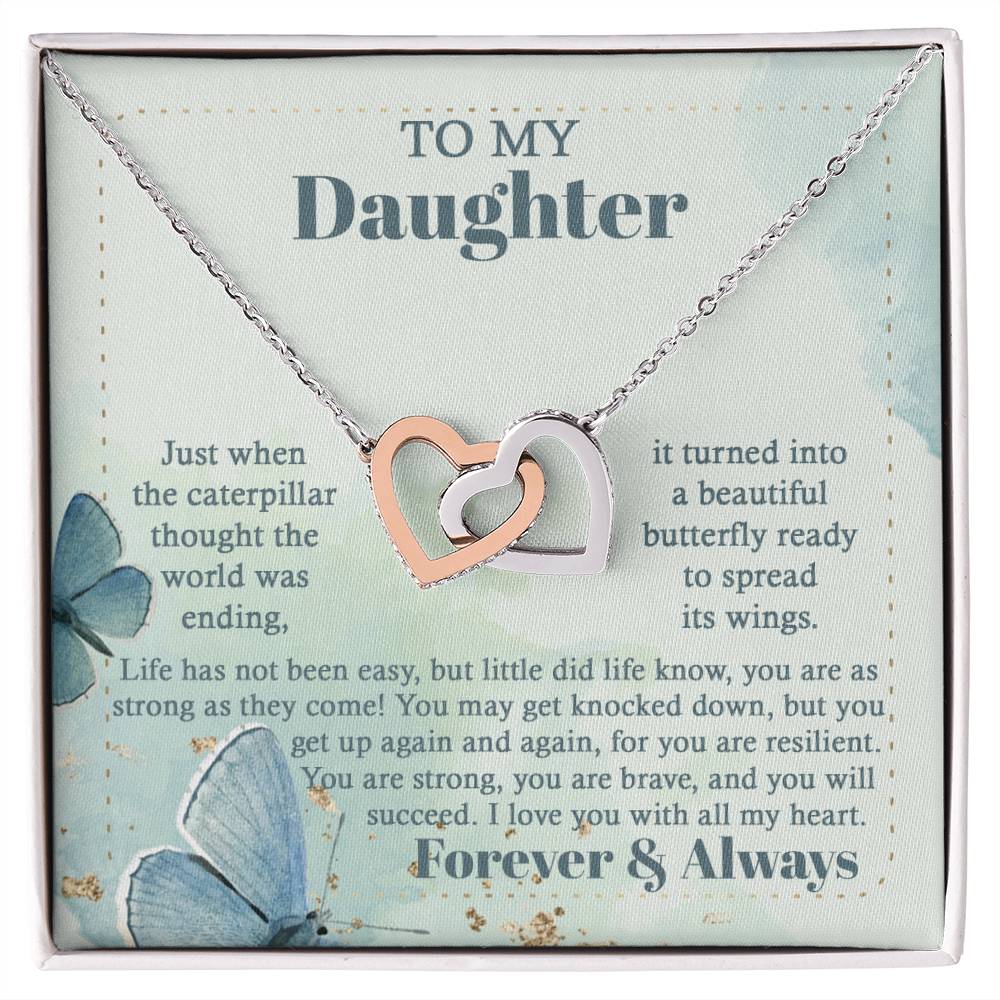 The "To Daughter, Beautiful Butterfly - Interlocking Hearts Necklace" is beautifully presented in a box adorned with blue butterflies and motivational messages about resilience and love. Sparkling with cubic zirconia crystals, this adjustable-length necklace ensures a perfect fit, making it a treasured keepsake for your daughter.