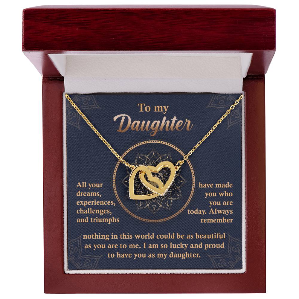 A "To My Daughter, All Your Dreams - Interlocking Hearts Necklace" with a rose gold finish and sparkling cubic zirconia crystals sits in a display box, accompanied by a heartfelt message expressing a parent's pride and love for their daughter.