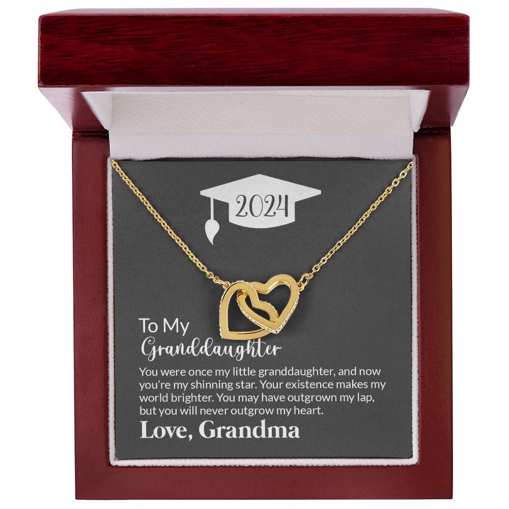 A ShineOn Fulfillment To My Granddaughter, Never Outgrow My Hearts - Interlocking Hearts Necklace with a graduation cap motif displayed in a gift box, featuring a sentimental inscription from a grandmother to her granddaughter for the year 2024.
