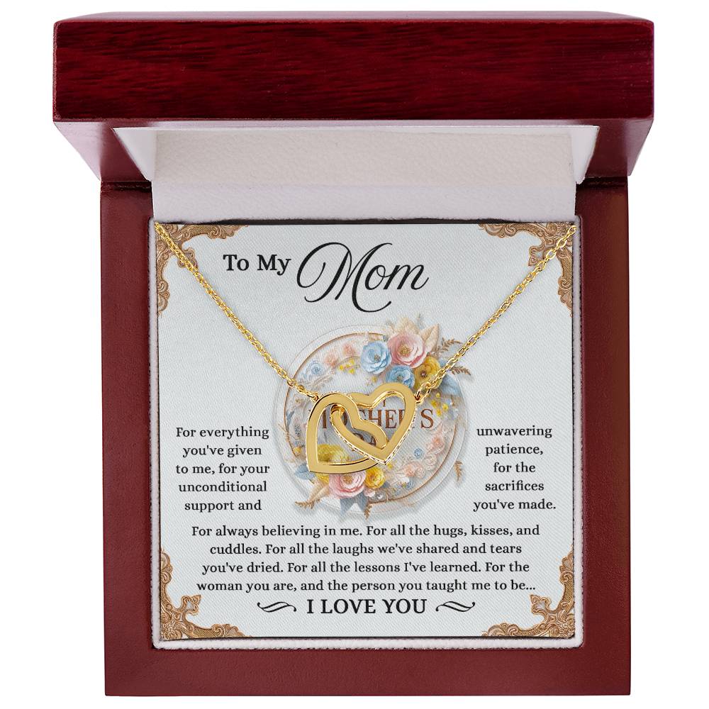 The Mom-Taught Me - Interlocking Hearts Necklace, finished in rose gold and shimmering with cubic zirconia crystals, is presented in an open red box. The background card features a heartfelt message for "Mom," thanking her for her support and sacrifices, beautifully adorned with floral accents.