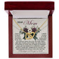 The Mom-Guardian Angel - Interlocking Hearts Necklace, featuring cubic zirconia crystals, rests in a jewelry box on a floral-themed "Dear Mom" card. It beautifully conveys gratitude and love for a mother's unwavering care, making it the perfect gift for her.
