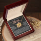 The Mom-More To Me 2 - Interlocking Hearts Necklace features heart-shaped pendants adorned with cubic zirconia crystals, presented in an open dark wood box. The lid reads: "To a wonderful Mom," with dried flowers as a graceful backdrop.