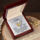 Inside a dark wooden jewelry box, the Daughter-An Angel - Interlocking Hearts Necklace with rose gold finish and cubic zirconia crystals is accompanied by a heartwarming engraved message to a daughter. Dried flowers adorn the wooden surface beside it.