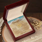 The Daughter-Ocean Waves - Interlocking Hearts Necklace, featuring a rose gold finish and cubic zirconia, is beautifully presented in an open wooden box on a rustic surface. The box includes a sentimental "To my Daughter" note, surrounded by dried flowers and a tree slice.