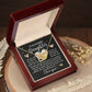 An open wooden jewelry box showcases the Daughter-Your Strength - Interlocking Hearts Necklace, its pendants sparkling with cubic zirconia. Behind it, a heartfelt message conveys love and support for a daughter, while dried flowers adorn the wooden surface.