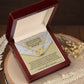 The Mother's Day-Thank You - Interlocking Hearts Necklace with sparkling cubic zirconia is displayed in a red box beside a thank you card for Mom, with dried flowers and white fern leaves on a wooden surface.