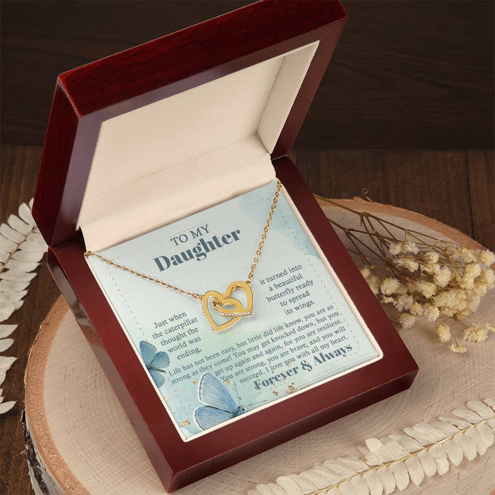 The "To Daughter, Beautiful Butterfly - Interlocking Hearts Necklace" is beautifully presented in a box adorned with blue butterflies and motivational messages about resilience and love. Sparkling with cubic zirconia crystals, this adjustable-length necklace ensures a perfect fit, making it a treasured keepsake for your daughter.