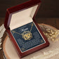 On a wooden surface, a jewelry box holds the Mom-Thankful Heart - Interlocking Hearts necklace in rose gold. The lid reads "To My Boyfriend's Mom" with a heartfelt message, complemented by dried flowers.