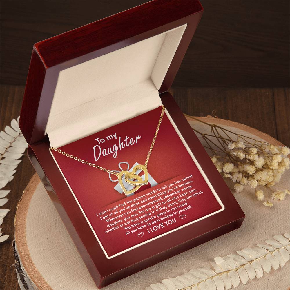 A stunning "To Daughter, A Gift - Interlocking Hearts Necklace" with cubic zirconia crystals is displayed on a red card, featuring a heartfelt message for a daughter, expressing pride, love, and encouragement.