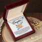 The Daughter-Brilliance Within - Interlocking Hearts Necklace, crafted from two-tone surgical steel and gold, is presented in an open jewelry box inscribed with "To My Dearest Daughter." Dried flowers nearby enhance its sentimental charm on the wooden surface.