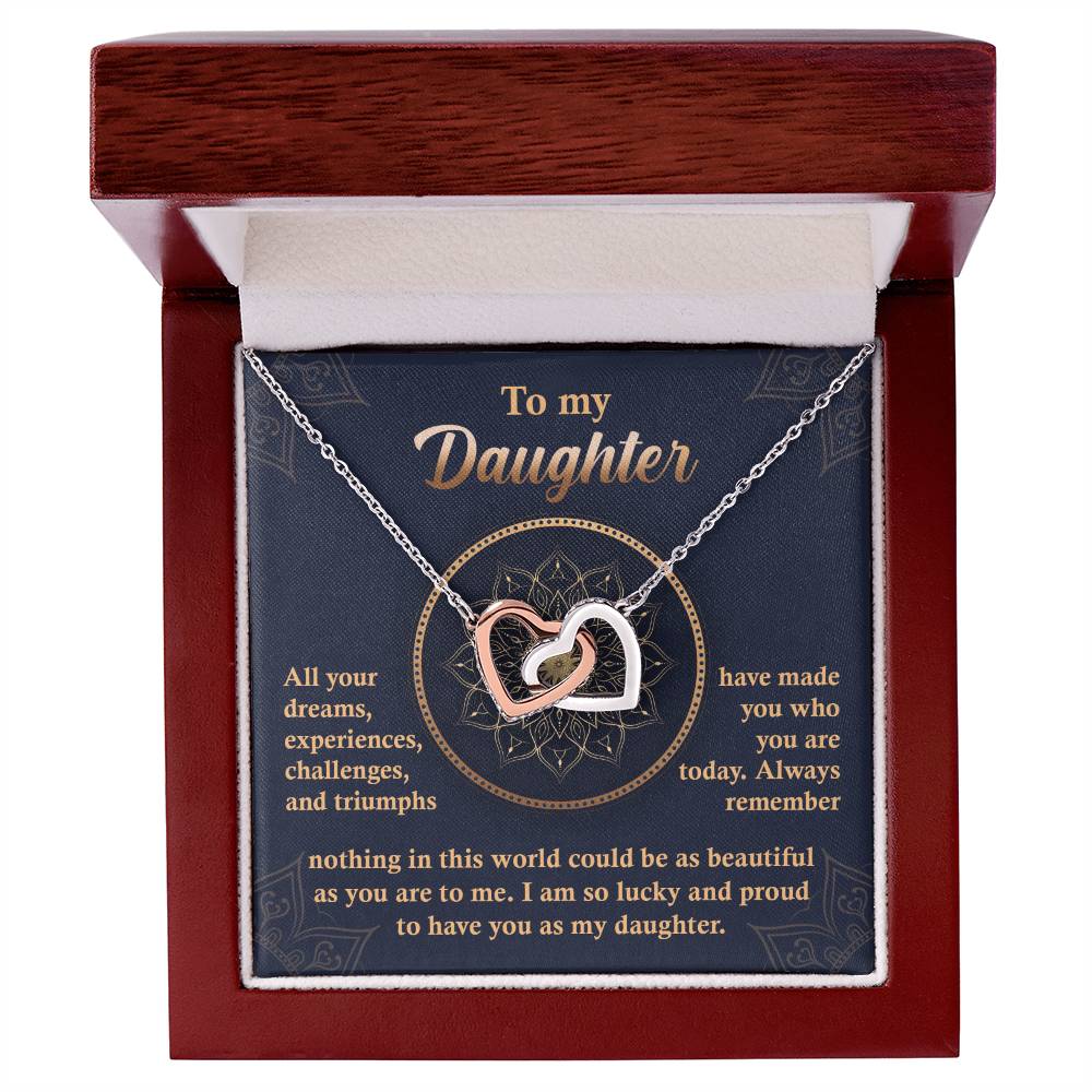 A "To My Daughter, All Your Dreams - Interlocking Hearts Necklace" with a rose gold finish and sparkling cubic zirconia crystals sits in a display box, accompanied by a heartfelt message expressing a parent's pride and love for their daughter.