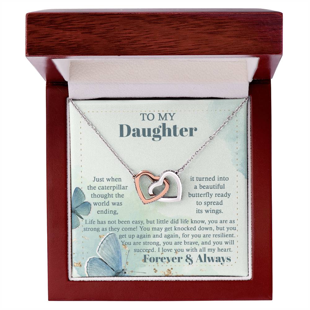 The "To Daughter, Beautiful Butterfly - Interlocking Hearts Necklace" is beautifully presented in a box adorned with blue butterflies and motivational messages about resilience and love. Sparkling with cubic zirconia crystals, this adjustable-length necklace ensures a perfect fit, making it a treasured keepsake for your daughter.