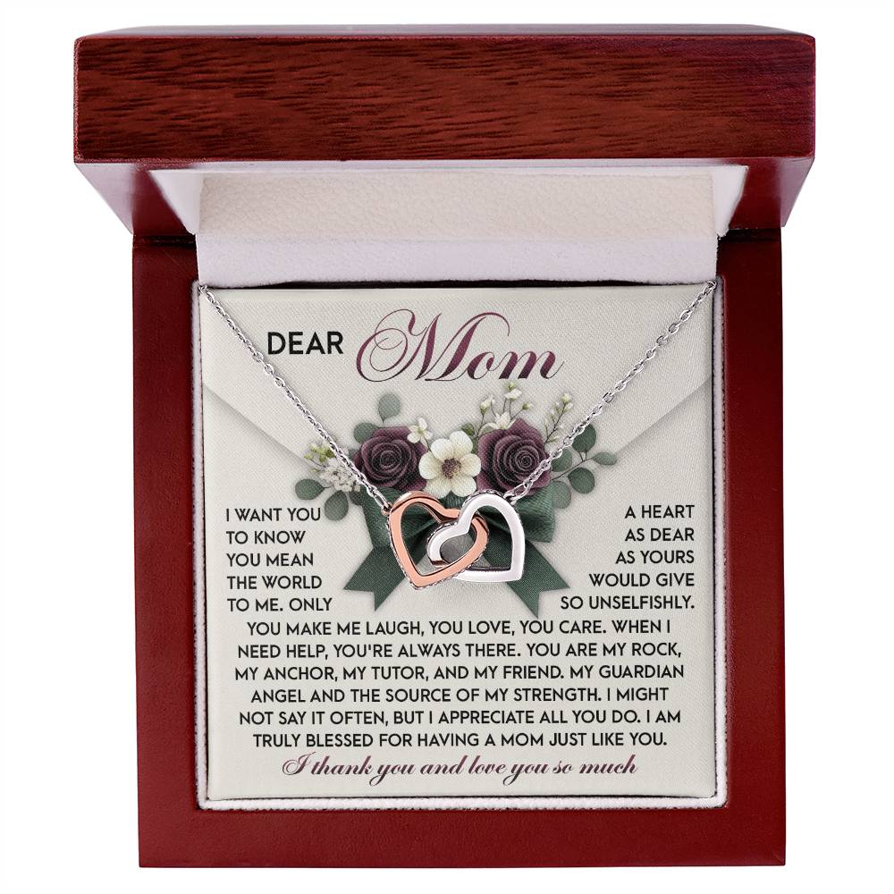 The Mom-Guardian Angel - Interlocking Hearts Necklace, embellished with sparkling cubic zirconia crystals, is elegantly presented in an open wooden box. Behind it, a heartfelt "Dear Mom" letter surrounded by floral designs conveys gratitude and admiration.