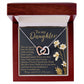 The Daughter-One Kind - Interlocking Hearts Necklace is a rose gold-finished piece adorned with cubic zirconia crystals. It comes in an open jewelry box displaying an inscription "To my Daughter," surrounded by decorative floral accents.