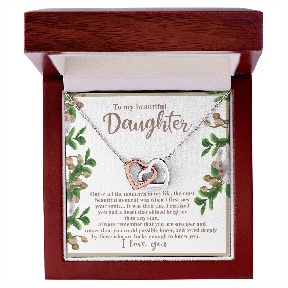 The Daughter-First Smile Interlocking Hearts Necklace, adorned with cubic zirconia crystals, arrives in a wooden box. Inside the lid, surrounded by floral decorations, is the heartfelt message "To my beautiful Daughter," celebrating love, strength, and grace.