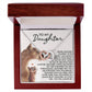 The Daughter-Never Alone - Interlocking Hearts Necklace, in a rose gold finish with cubic zirconia crystals, rests on a white cushion in a wooden box. The cushion has a cat and kitten illustration and expresses love from parent to daughter.