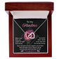 The Grandma-Love For Me - Interlocking Hearts Necklace, featuring a silver heart-shaped pendant with cubic zirconia crystals, comes in a wooden box. The lid has "To my Grandma" above a pink rose graphic, conveying gratitude and love for her unwavering support and guidance.