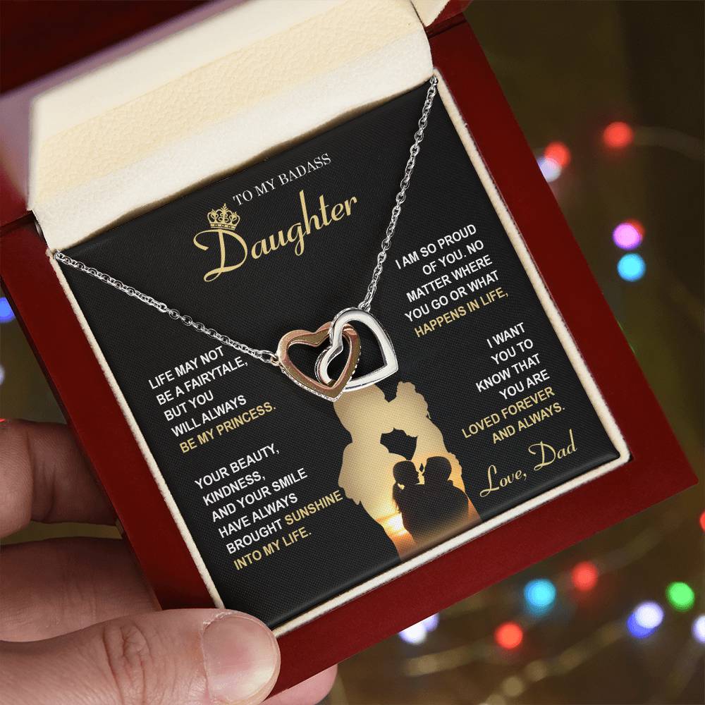 The "To Daughter, Be My Princess - Interlocking Hearts Necklace" with a rose gold finish and adorned with cubic zirconia crystals is displayed in a box that features a heartfelt message from a father to his daughter about love, support, and pride. The text and silhouette of a father and daughter are also included below.