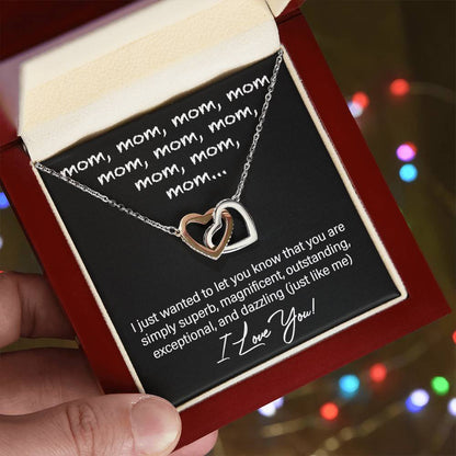 A hand holds an open jewelry box revealing the "To Mom, Just Like Me - Interlocking Hearts Necklace" adorned with cubic zirconia crystals and a heart-shaped pendant inscribed with repeated praises for "mom," expressing love—a perfect personalized gift.