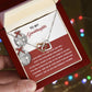 An open red jewelry box is held in a hand, displaying the "Granddaughter-To An End - Interlocking Hearts Necklace" crafted in surgical steel with a rose gold finish. Inside, a heartfelt printed message dedicated to a granddaughter enhances the gift's sparkle and symbolizes the enduring nature of their bond.