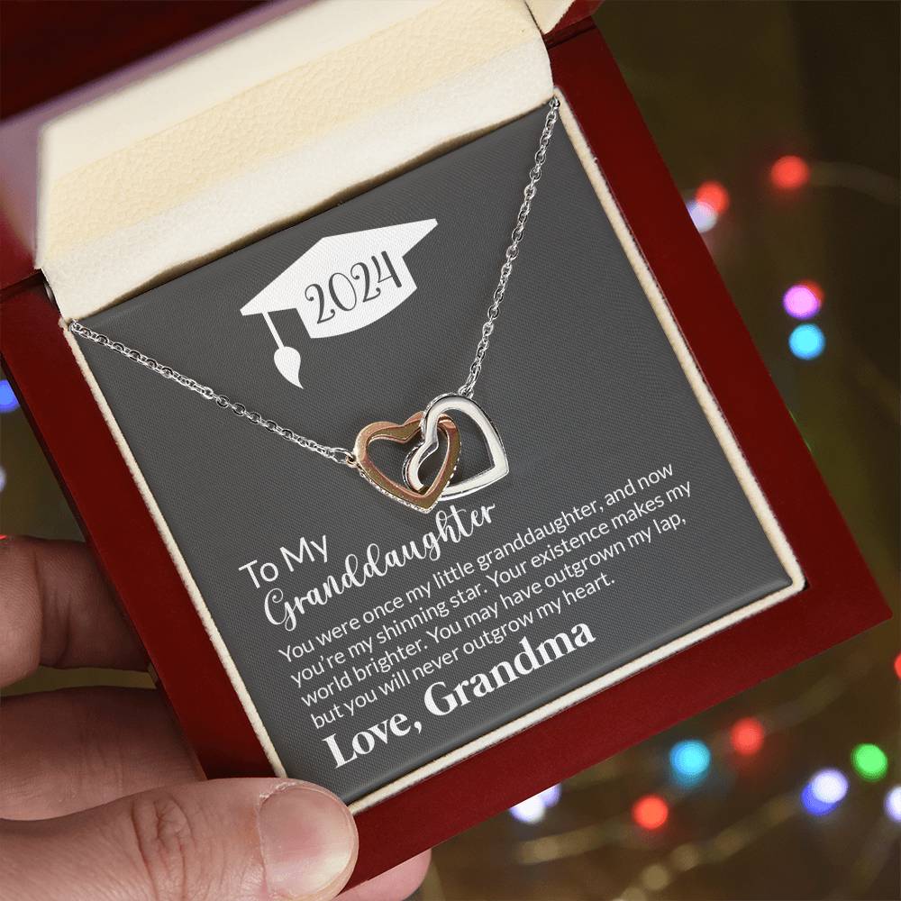 A hand holding an anniversary gift box with a "To My Granddaughter, Never Outgrow My Hearts" Interlocking Hearts Necklace from ShineOn Fulfillment and a sentimental note from a grandmother to her granddaughter.