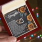 A person holds an open gift box revealing a stunning Daughter-Loved Enough - Interlocking Hearts Necklace, crafted with shimmering cubic zirconia crystals. Behind the necklace is a heartfelt message titled "To My Beautiful Daughter," adorned with golden roses, as festive lights softly blur in the background.