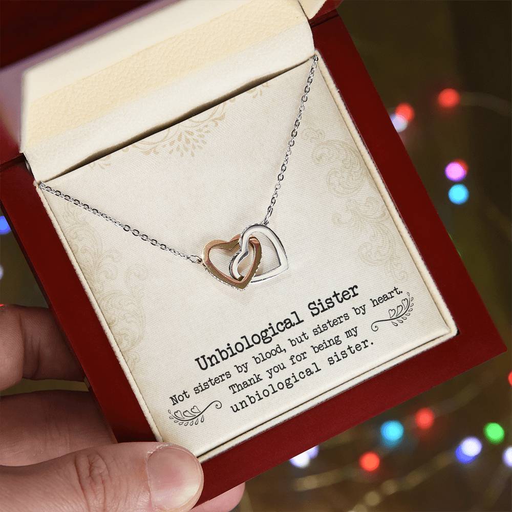 A hand holding a red gift box with a To My Unbiological Sister, Sister By Heart - Interlocking Hearts Necklace inscribed with the words "unbiological sister" from ShineOn Fulfillment.