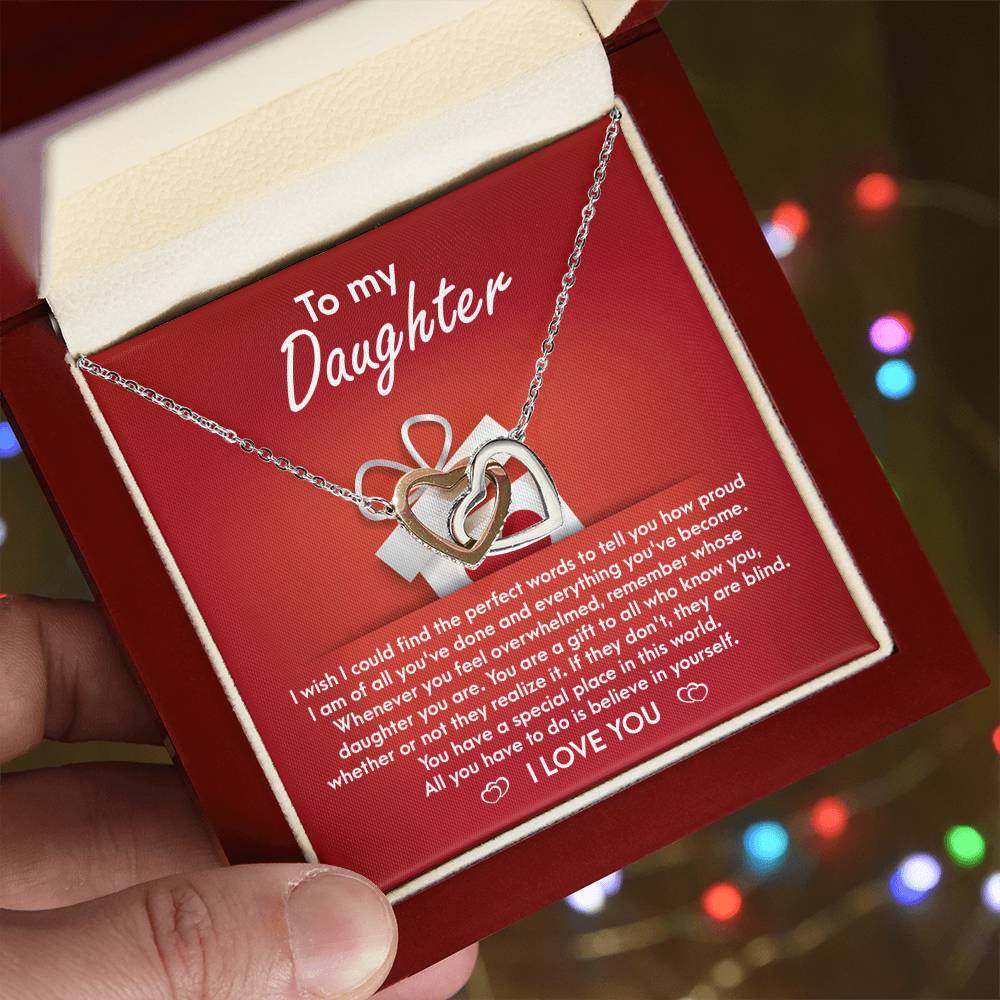 A stunning "To Daughter, A Gift - Interlocking Hearts Necklace" with cubic zirconia crystals is displayed on a red card, featuring a heartfelt message for a daughter, expressing pride, love, and encouragement.