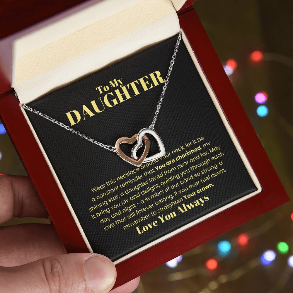The "[Almost Sold Out] To My Daughter, Wear This Necklace - Interlocking Hearts Necklace" features intertwined hearts adorned with sparkling cubic zirconia crystals. It is beautifully displayed in a red jewelry box against a black background, accompanied by a heartfelt message symbolizing eternal love.