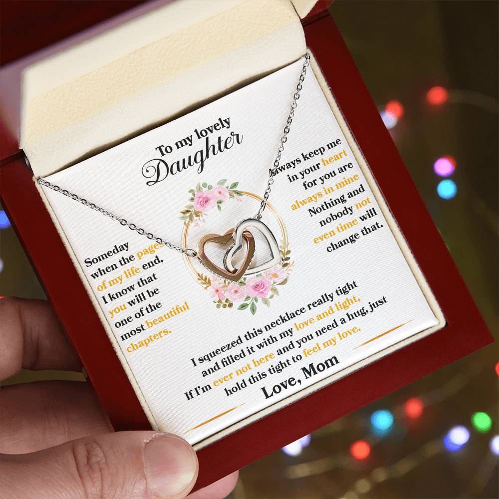 A hand holding a gift box with a "To My Lovely Daughter, Hold This Tight To Feel My Love" Interlocking Hearts necklace from ShineOn Fulfillment and a heartfelt message to a daughter from a mother.