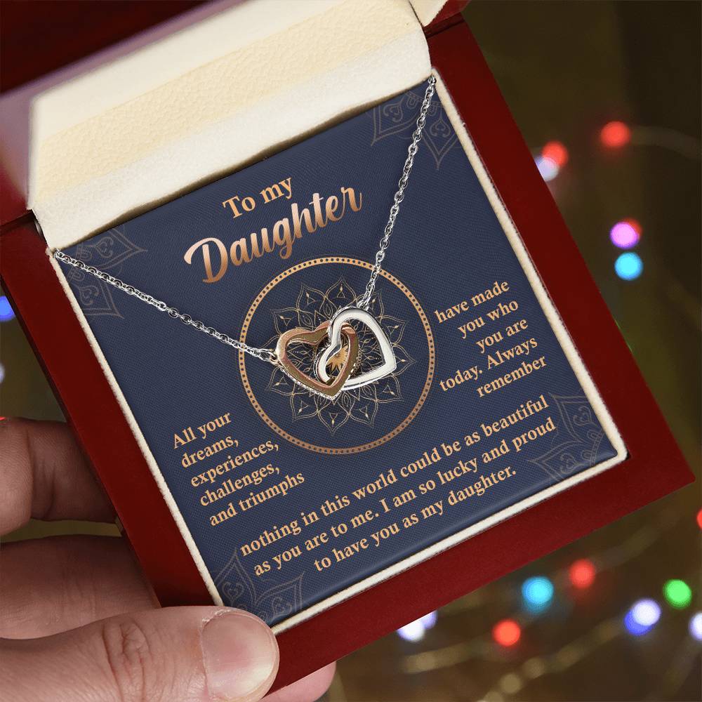 A "To My Daughter, All Your Dreams - Interlocking Hearts Necklace" with a rose gold finish and sparkling cubic zirconia crystals sits in a display box, accompanied by a heartfelt message expressing a parent's pride and love for their daughter.