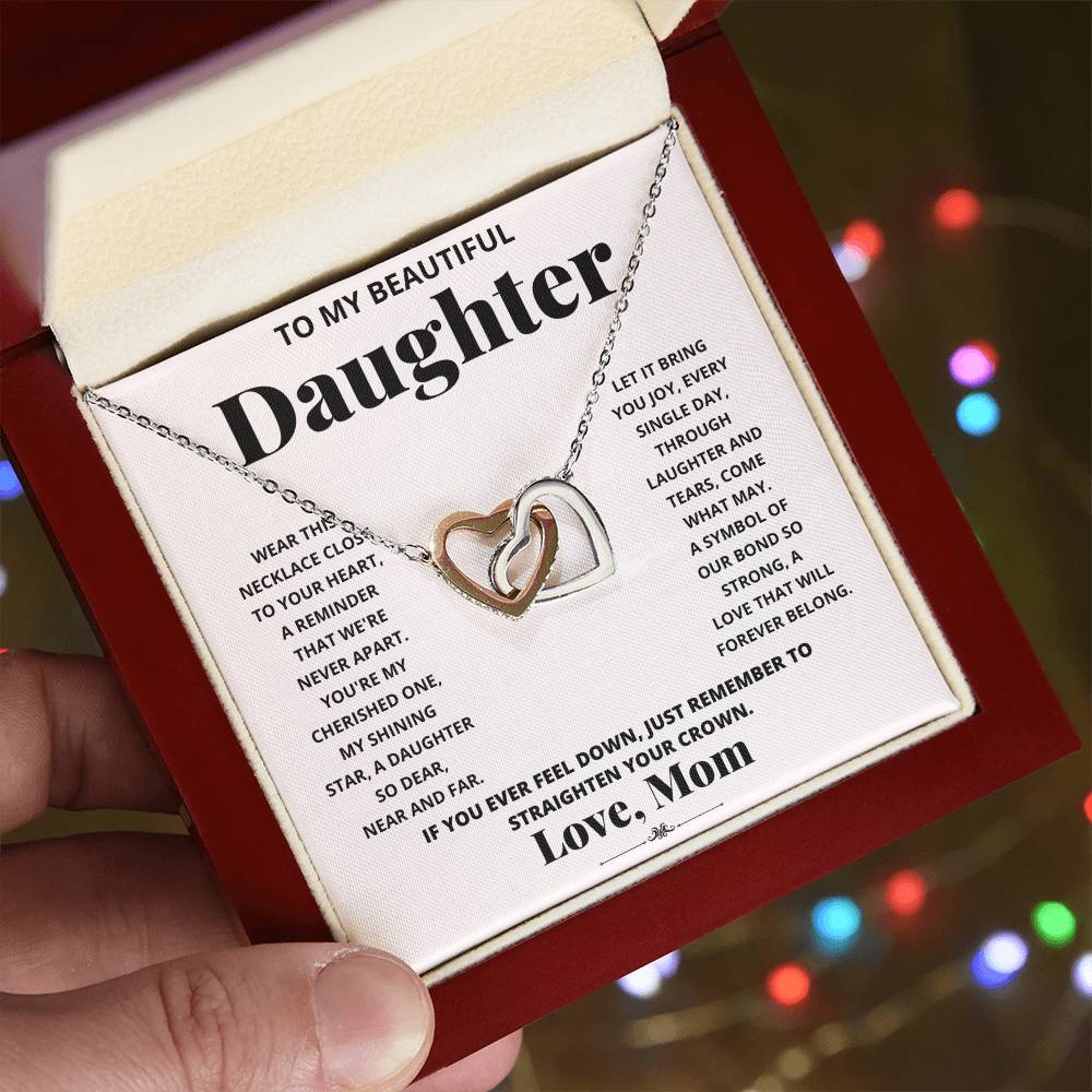 A "To My Beautiful Daughter, Wear This Necklace - Interlocking Hearts Necklace" with interlocking hearts pendants adorned with cubic zirconia crystals, presented in a box with a heartfelt message from a mother to her daughter.
