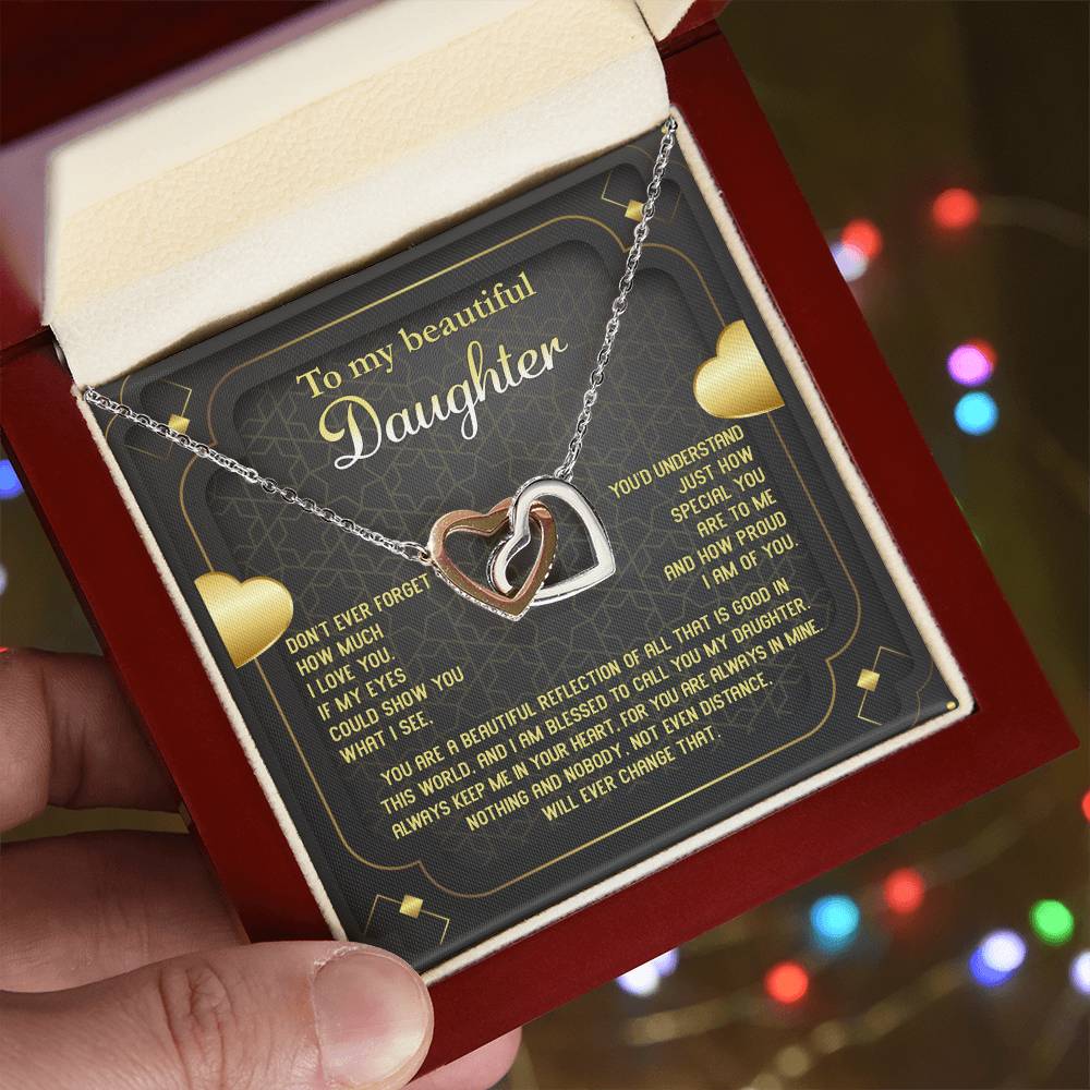 The "To Daughter, Beautiful Reflection - Interlocking Hearts Necklace" features an 18k yellow gold finish and is presented on a card that conveys a heartfelt message of love, pride, and eternal connection. The interlocking hearts are adorned with sparkling cubic zirconia crystals.