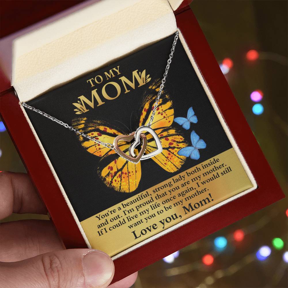 An open jewelry box reveals the "[Almost Sold Out] To Mom, Strong Lady - Interlocking Hearts Necklace" with sparkling cubic zirconia crystals. A card with a butterfly design and heartfelt message for "Mom" is in the background, making it a cherished unique gift.