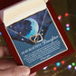 A hand holds a red box with an Interlocking Hearts Necklace in rose gold. A message card featuring a moon and stars reads, "To My Beautiful Daughter," expressing love and pride. Cubic zirconia crystals add sparkle to blurred background lights. Product: Daughter-Grown Heart - Interlocking Hearts Necklace.
