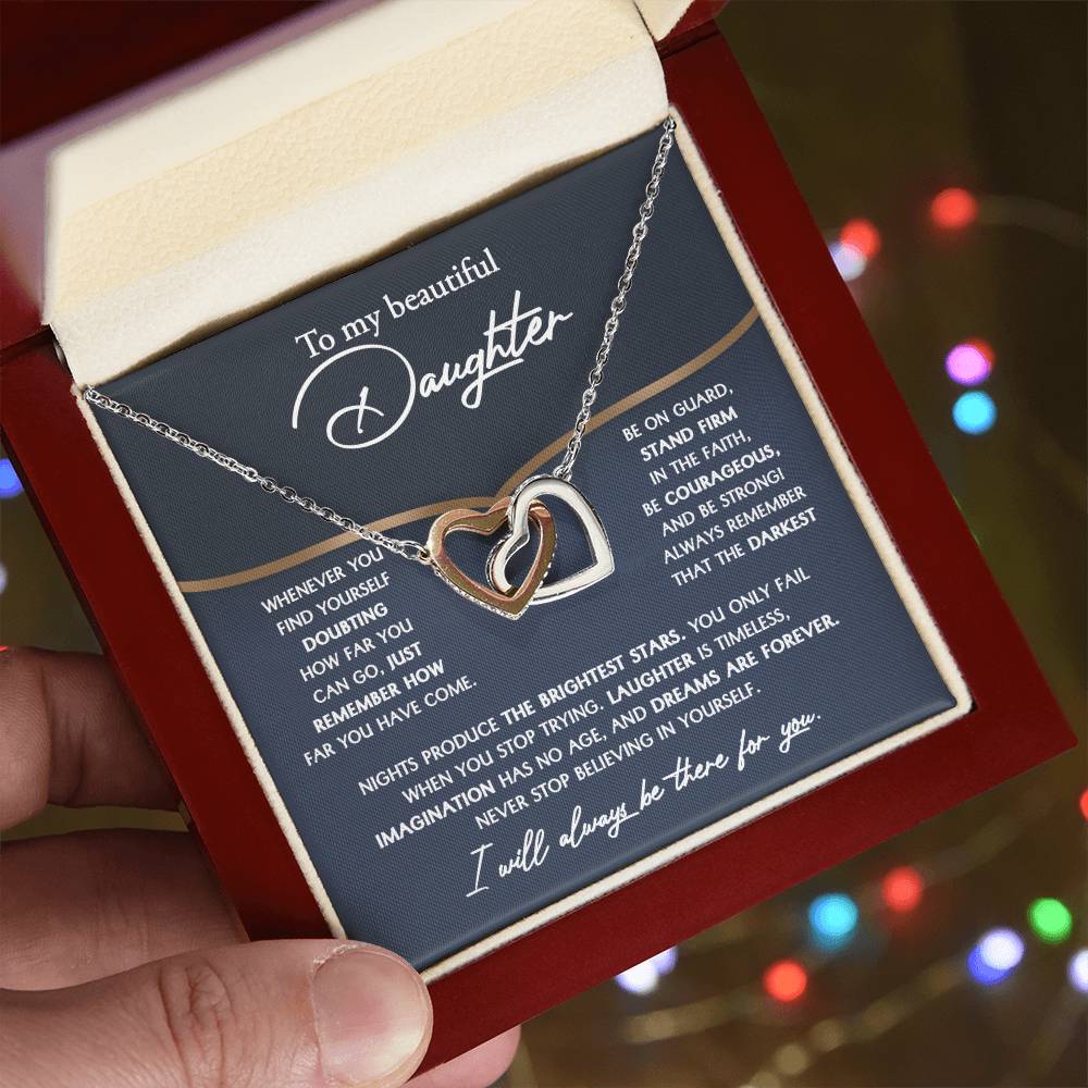 The "To Daughter, Brightest Stars - Interlocking Hearts Necklace," crafted from high-quality polished surgical steel and adorned with cubic zirconia crystals, is presented on a message card addressed to a daughter, offering encouraging and motivational words.