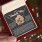 A person holds an open red gift box showing the Mom-More To Me - Interlocking Hearts necklace, finished in rose gold with cubic zirconia crystals. The inside lid has a heartfelt message for a "Wonderful Mom" in white script, while colorful lights shimmer blurred in the background.