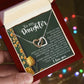 The Daughter-Tough Days Interlocking Hearts necklace, with a rose gold finish, comes in a red box. The lid has a heartfelt message for daughters and an illustration of yellow flowers, while twinkling lights create a soft background ambiance.