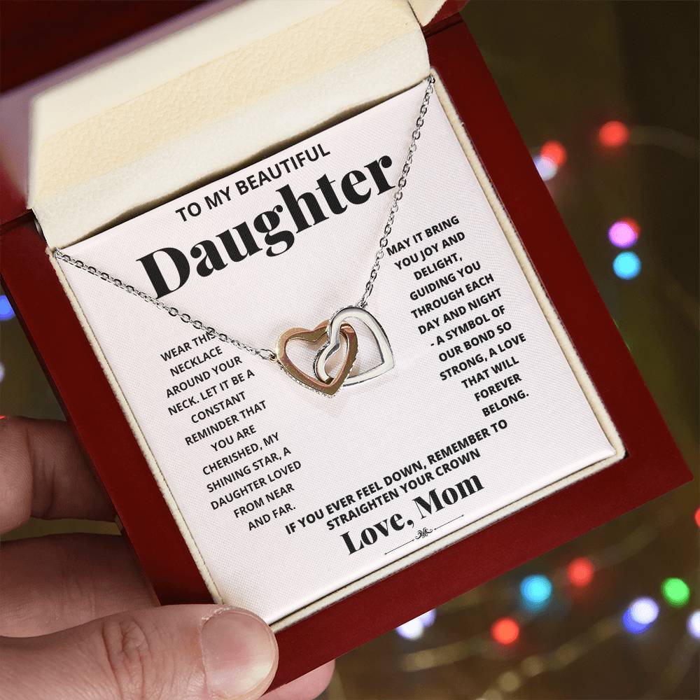 A "To My Daughter, Wear This Necklace - Interlocking Hearts Necklace" with interlocking heart pendants adorned with cubic zirconia crystals on a printed message card from a mother to her daughter, expressing love and encouragement.