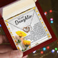 A hand holds an open jewelry box displaying the Daughter-Journey Home Interlocking Hearts Necklace with cubic zirconia. The box, featuring a "To My Daughter" message, is designed with yellow flowers on a white background, against softly blurred multicolored lights.