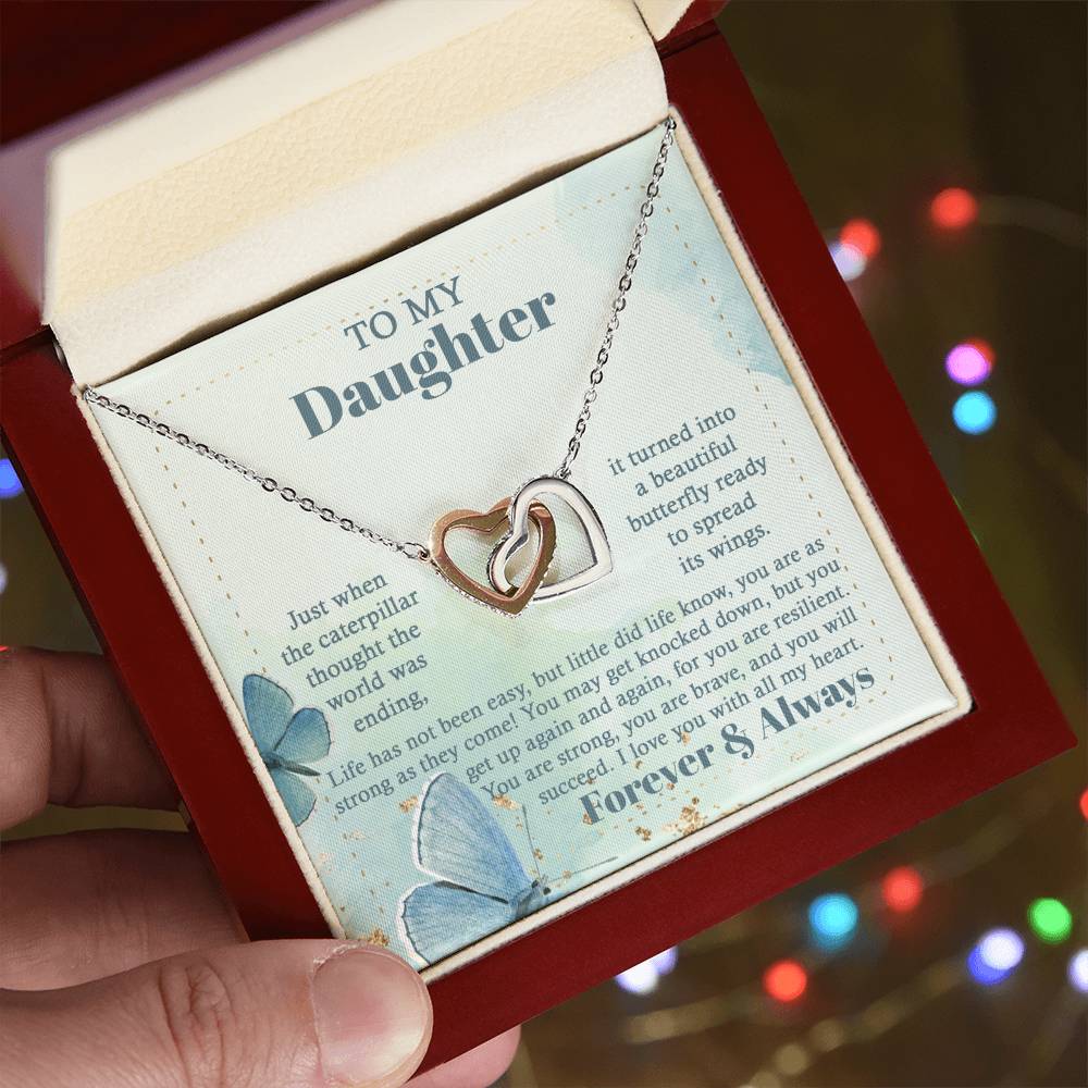 The "To Daughter, Beautiful Butterfly - Interlocking Hearts Necklace" is beautifully presented in a box adorned with blue butterflies and motivational messages about resilience and love. Sparkling with cubic zirconia crystals, this adjustable-length necklace ensures a perfect fit, making it a treasured keepsake for your daughter.