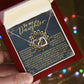 A person holds an open box displaying the Daughter-Reach Stars Interlocking Hearts necklace with cubic zirconia. The lid bears a heartfelt message to a daughter, exuding love and encouragement, while blurred colorful lights create a warm background glow.