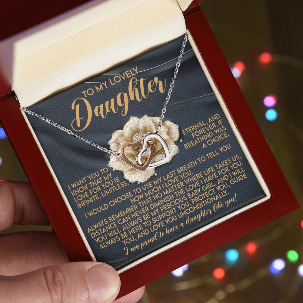 A hand reveals an open jewelry box with a Daughter-Infinite Love - Interlocking Hearts Necklace adorned in cubic zirconia. "To My Lovely Daughter" is inscribed inside, followed by a heartfelt message of love and pride, set against a soft floral background.